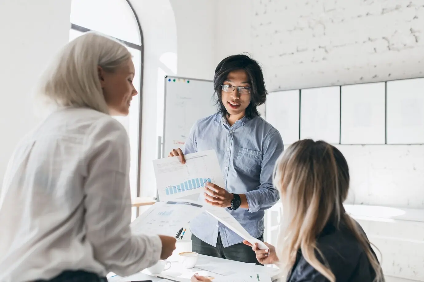 Gutaussehender asiatischer Student erklärt seinen Kommilitonen, die wirtschaftliche Diagramme halten, etwas.